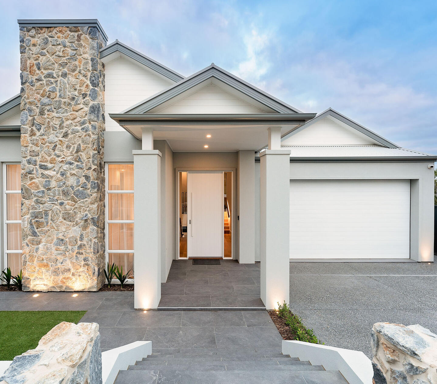 A modern house with a stylish stone pillar, sleek neutral walls, a grand entrance, and a spacious driveway leading to a double garage, showcasing knock down rebuild construction.